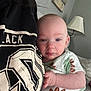 baby, infant, person, clothing, black_shirt, print, hand, face, living_room, lamp, wall_art, couch, home_interior, casual, portrait, skin, comfort, holding, young_child, indoor