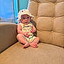 baby, child, hat, white_hat, bear_face, sitting, curious, beige_chair, cushion, indoor, window, natural_light, skin, feet, arms, clothing, infant, cute, face, portrait