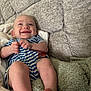 baby, smiling, striped_clothing, couch, blanket, infant, happy, person, indoor, skin, head, legs, feet, hand, cozy, texture, soft, comfort, child, young