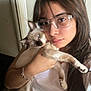 Pancho is registered to the contest to win money with this photo: person, cat, indoor, glasses, long_hair, white_shirt, bracelet, siamese_cat, holding, face, pet, cute, closeup, looking_at_camera, feline, young_adult, animal, human, portrait, cozy
