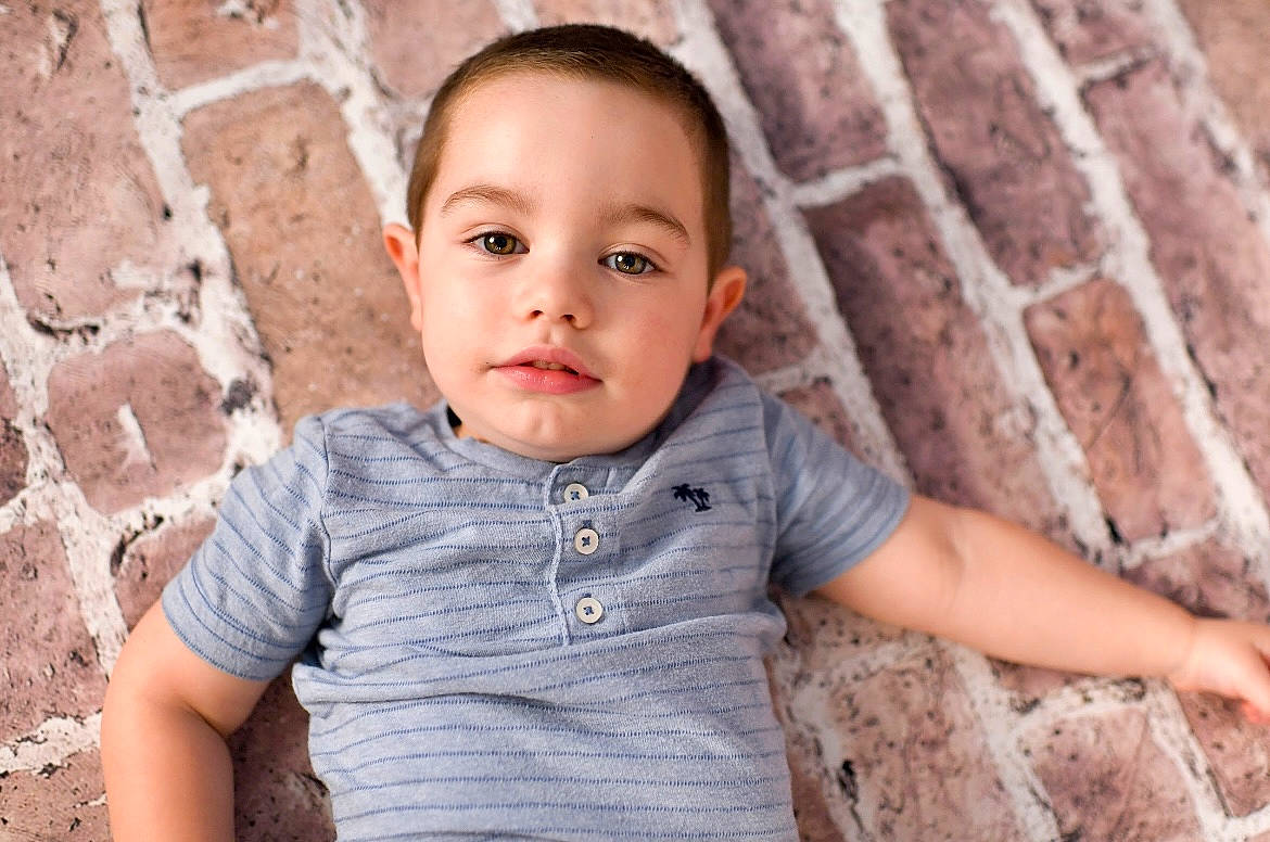 Frankie is registered to the contest to win money with this photo: baby, baby_toddler_clothing, brick, cheek, child, chin, eye, face, flash_photography, hair, happy, nose, person, plant, sitting, skin, sleeve, t_shirt, toddler, tree