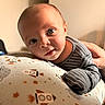 baby, infant, face, blue_eyes, clothing, striped_shirt, hand, cushion, space_theme, rocket, stars, planet, indoor, portrait, child, resting, curious, smile, person, closeup