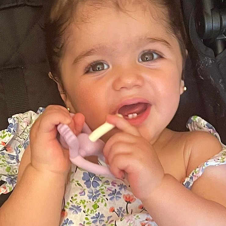 Aleyna is registered to the contest to win money with this photo: baby, chewing, child, closeup, cute, female, floral_dress, hair_tie, hand, happy, indoors, infant, person, portrait, seatbelt, skin, smiling, stroller, teething_toy, young_child