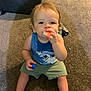 Ozzee is registered to the contest to win money with this photo: toddler, child, carpet, indoor, blue_tank_top, shark_design, green_shorts, barefoot, shoe, toy_ball, snack, curly_hair, sitting, looking_at_camera, person, floor, casual_clothing, young_child, cute, home