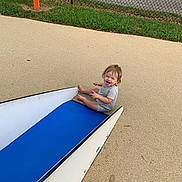 Ozzee joined the competition — help win amazing prizes! toddler, child, slide, playground, happy, laughing, outdoor, grass, fence, sign, blue_slide, sand, play, fun, summer, casual_clothing, short_sleeves, barefoot, person, daytime