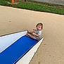 toddler, child, slide, playground, happy, laughing, outdoor, grass, fence, sign, blue_slide, sand, play, fun, summer, casual_clothing, short_sleeves, barefoot, person, daytime