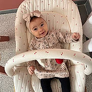 Lucy a rejoint le concours — aidez-le/la à gagner de superbes lots ! baby, child, infant, headband, bow, dress, patterned_clothing, black_tights, baby_seat, cushion, cherry_pattern, smiling, happy, indoors, floor_pattern, pink_wall, power_socket, furniture, toy_bar, portrait