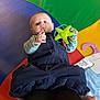 baby, blue_shirt, child, clothing, colorful_mat, feet, floor, green_toy, holding, indoor, infant, legs, looking_up, overalls, person, playtime, star_shaped_toy, striped_sleeves, toy, wooden_floor