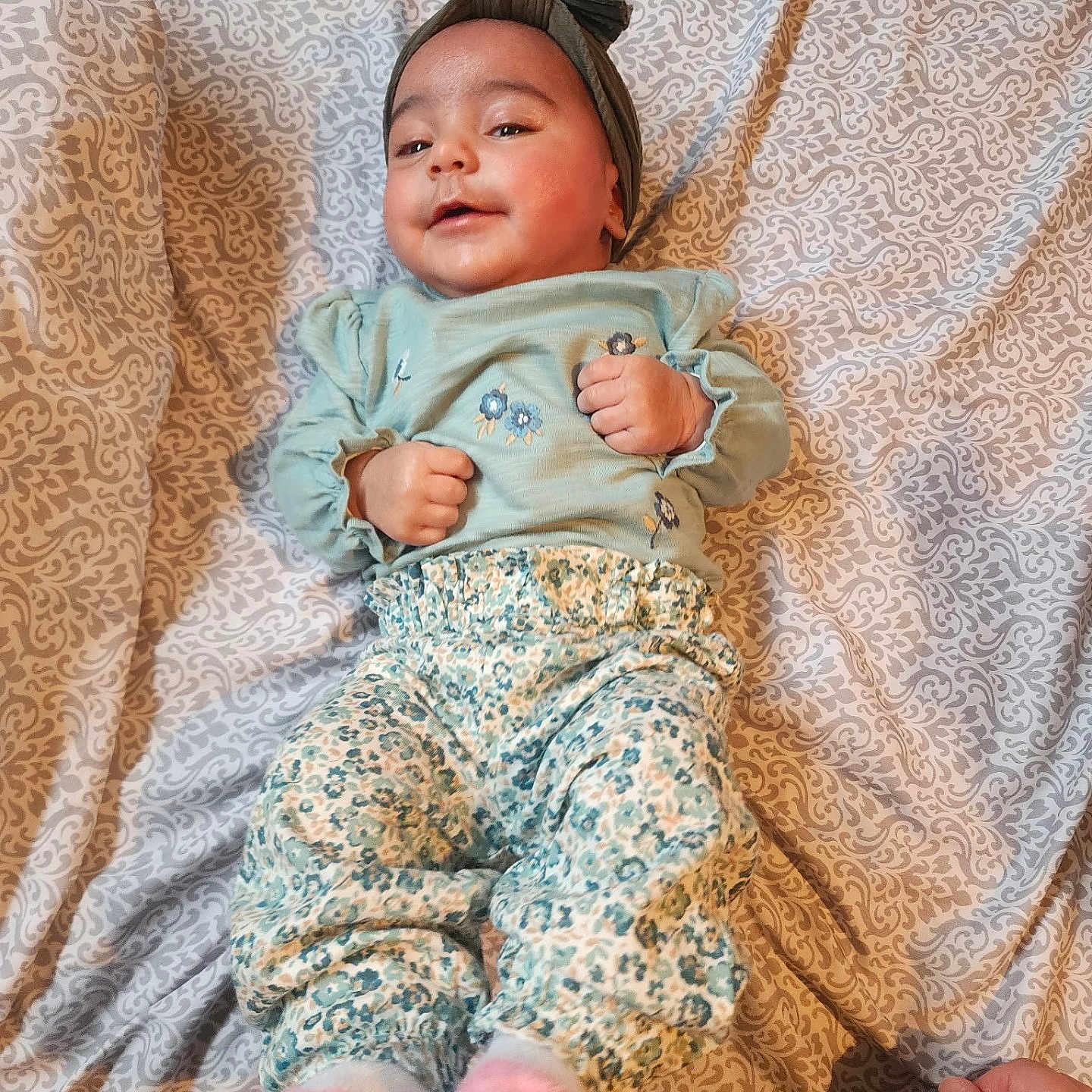 Inaya is registered to the contest to win money with this photo: baby, bed, blanket, child, clothing, cozy, cute, fabric, hand, headband, home, infant, lying_down, pants, pattern, person, relaxed, smile, socks, soft