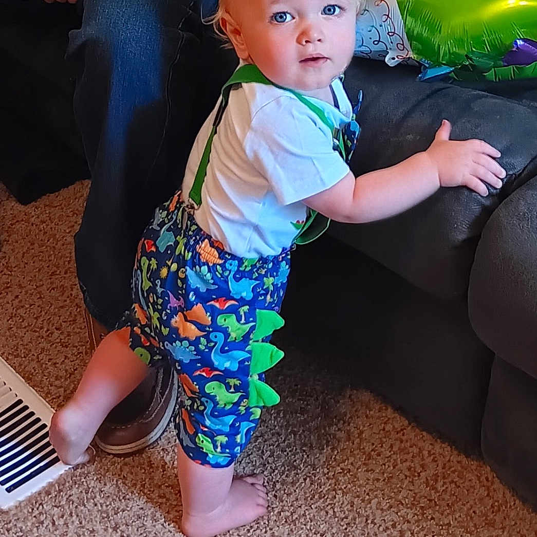 Rhett joined the competition — help win amazing prizes! adult, baby, blue_eyes, carpet, child, clothing, colorful, couch, curious, dinosaur_shorts, foot, furniture, hand, home, indoor, person, shorts, standing, suspenders, toddler