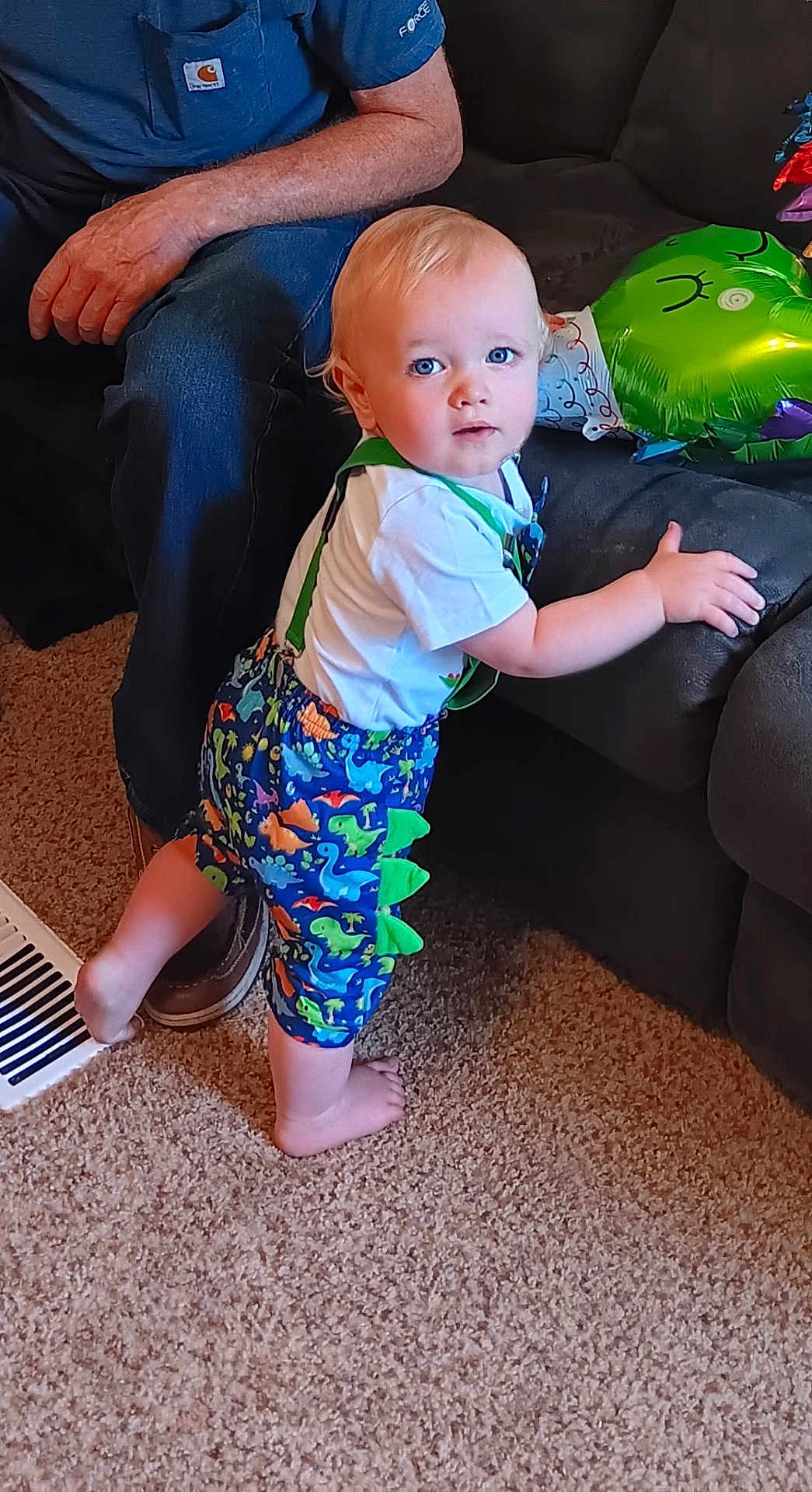 Rhett joined the competition — help win amazing prizes! toddler, child, blue_eyes, dinosaur_shorts, carpet, couch, indoor, person, adult, hand, foot, clothing, standing, home, furniture, colorful, shorts, suspenders, curious, baby