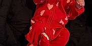 Jourmani is registered to the contest to win money with this photo: baby, infant, red_onesie, hearts, black_blanket, lying_down, tongue_out, cute, sleepwear, newborn, small_hands, footed_pajamas, playful, child, indoors, cozy, soft_fabric, person, resting, adorable