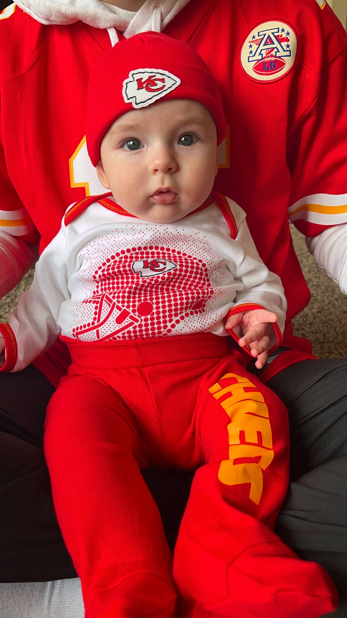 Bodie joined the competition — help win amazing prizes! baby, baby_toddler_clothing, cap, child, costume_hat, event, face, facial_expression, happy, hat, headwear, holiday, outerwear, person, red, santa_claus, sitting, sleeve, t_shirt, thigh