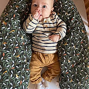 Félix participe au concours pour gagner de l'argent avec cette photo : baby, infant, child, newborn, striped_shirt, mustard_pants, socks, nursing_pillow, floral_pattern, bird_pattern, bedding, wooden_cradle, lying_down, hand_in_mouth, big_eyes, smiling, portrait, cozy, indoor, baby_furniture