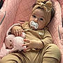 baby, infant, pacifier, headband, bow, stuffed_animal, pink, quilted, baby_seat, clothing, socks, tan_outfit, cute, child, indoor, portrait, relaxed, person, soft_toy, comfortable
