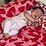 baby, sleeping, bed, blanket, heart_pattern, pink, red, clothing, infant, cute, cozy, peaceful, toddler, face, hand, foot, indoors, soft, comfort, portrait