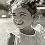 child, smiling, laughing, girl, hair_buns, outdoor, sunlight, dress, flower_pattern, happy, portrait, cute, young_child, natural_light, black_and_white, fashion, childhood, joy, person, closeup