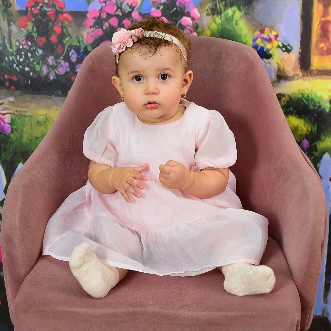 Emna Zina a rejoint le concours — aidez-le/la à gagner de superbes lots ! baby, chair, child, colorful_background, curly_hair, cute, decor, expression, floral, flower, furniture, girl, headband, indoor, pink_dress, portrait, seated, socks, studio_photo, wooden_floor
