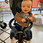 Noé participe au concours pour gagner de l'argent avec cette photo : baby, child, tricycle, smile, indoor, toy, person, seatbelt, carpet, window, chair, box, floor, hand, clothing, sock, furniture, curtain, happy, playtime