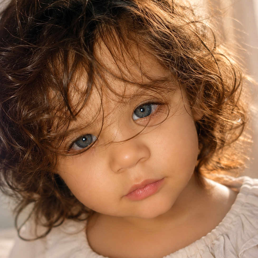 Ahitana. is registered to the contest to win money with this photo: blue_eyes, child, close_up, curly_hair, cute, expression, eyelashes, face, head, innocent, mouth, natural_light, nostrils, portrait, skin, soft_light, toddler, white_clothing, young_child