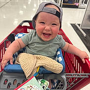 Jax joined the competition — help win amazing prizes! baby, shopping_cart, smiling, cap, green_shirt, blanket, book, store, aisle, shelves, toy, child, happy, indoor, retail, clothing, person, seat, cute, laughter