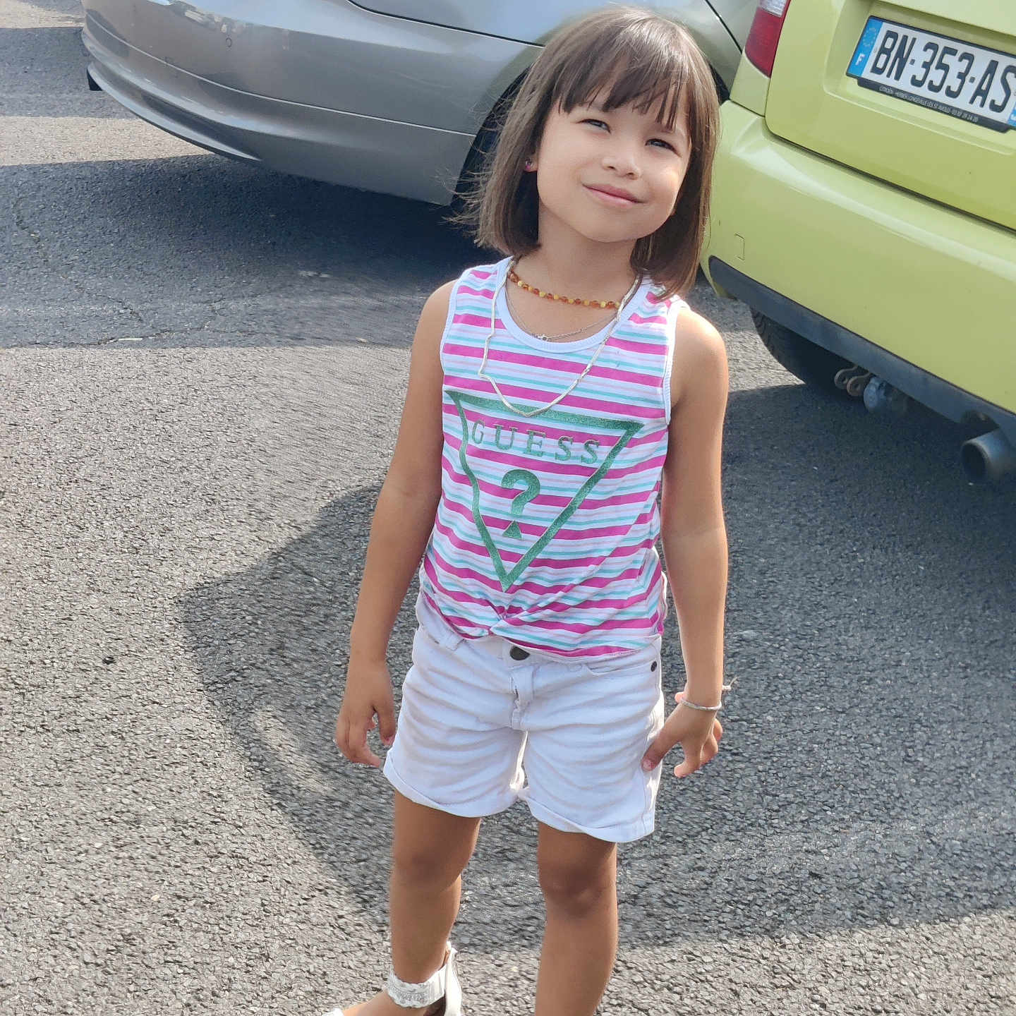 Nila participe au concours pour gagner de l'argent avec cette photo : asphalt, bracelet, car, casual_clothing, child, cute, daylight, fashion, girl, happy, necklace, outdoor, parking_lot, portrait, sandals, shorts, smiling, standing, summer, tank_top