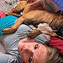 affection, animal, bed, blanket, casual_clothing, closeup, comfort, dog, face, friendship, hair, head, indoor, lying_down, paw, person, relaxation, resting, skin, tattoo