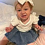 toddler, child, baby, headband, bow, denim_skirt, white_shirt, bed, pillow, blanket, smiling, funny_face, indoor, person, cute, sitting, clothing, skin, hair, happy