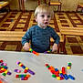 child, toddler, building_blocks, table, chair, floor, indoor, play, toy, colorful, wooden_furniture, patterned_floor, person, young_child, casual_clothing, activity, learning, education, curious, seated