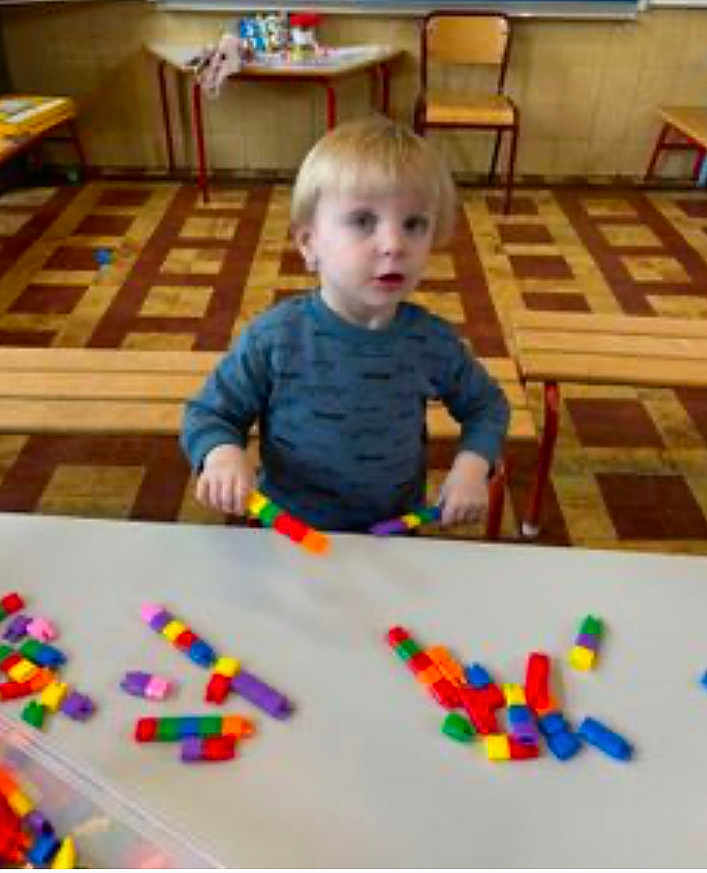 Alessio a rejoint le concours — aidez-le/la à gagner de superbes lots ! child, toddler, building_blocks, table, chair, floor, indoor, play, toy, colorful, wooden_furniture, patterned_floor, person, young_child, casual_clothing, activity, learning, education, curious, seated