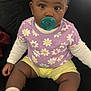 baby, child, pacifier, purple_shirt, daisy_pattern, yellow_shorts, white_socks, bows, pom_poms, sitting, couch, indoor, cute, infant, portrait, black_background, hand, feet, clothing, face