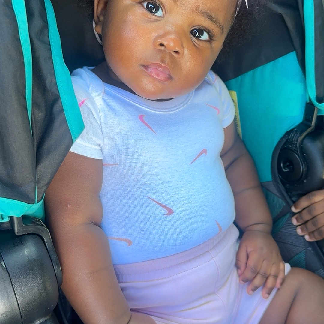 Jalani joined the competition — help win amazing prizes! baby, baby_clothes, black_skin, child, clothing, curly_hair, cute, expression, hand, headband, infant, legs, outdoor, pink_bow, portrait, shorts, sitting, stroller, sunlight, white_shirt