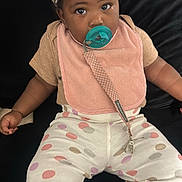 Jalani is registered to the contest to win money with this photo: baby, child, pacifier, bib, polka_dot, pants, bow, headwear, indoor, sitting, cute, infant, clothing, comfort, black_background, young_child, portrait, adorable, looking_at_camera, skin