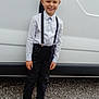 child, boy, smile, standing, suspenders, shirt, black_pants, shoes, vehicle, van, gravel, outdoor, casual, happy, portrait, person, hair, face, clothing, daylight