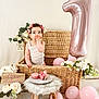 baby, flower_crown, wicker_basket, pink_balloon, number_one_balloon, macarons, plate, stool, flowers, birthday, celebration, cute, infant, white_background, decor, pink, child, sitting, indoors, portrait