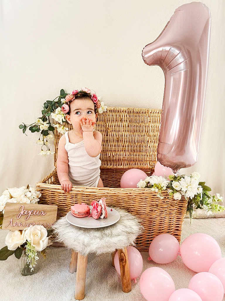 Amaia participe au concours pour gagner de l'argent avec cette photo : baby, flower_crown, wicker_basket, pink_balloon, number_one_balloon, macarons, plate, stool, flowers, birthday, celebration, cute, infant, white_background, decor, pink, child, sitting, indoors, portrait