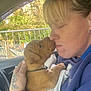 woman, puppy, dog, car_interior, tattoo, towel, close_up, affection, nose_touch, casual_clothing, blonde_hair, natural_light, window, hand, pet, cute, outdoor_background, seat, collar, intimate_moment