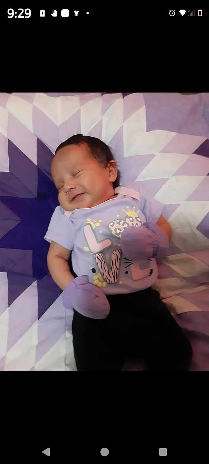 Kailecelove is registered to the contest to win money with this photo: baby, infant, sleeping, smile, mittens, purple, shirt, pattern, quilt, geometric_pattern, bed, child, cute, happy, relaxing, portrait, small_person, soft_lighting, indoor, resting
