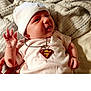 Persephone joined the competition — help win amazing prizes! baby, infant, white_hat, superman_necklace, blanket, hand, smile, cute, soft_lighting, indoors, skin, clothing, person, portrait, lying_down, newborn, cute_expression, child, young, accessory