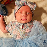 Persephone is registered to the contest to win money with this photo: baby, infant, child, floral_outfit, headband, bow, tutu, blue_tulle, clothing, closeup, portrait, laying_down, soft_surface, cute, young_child, person, indoors, face, expression, newborn