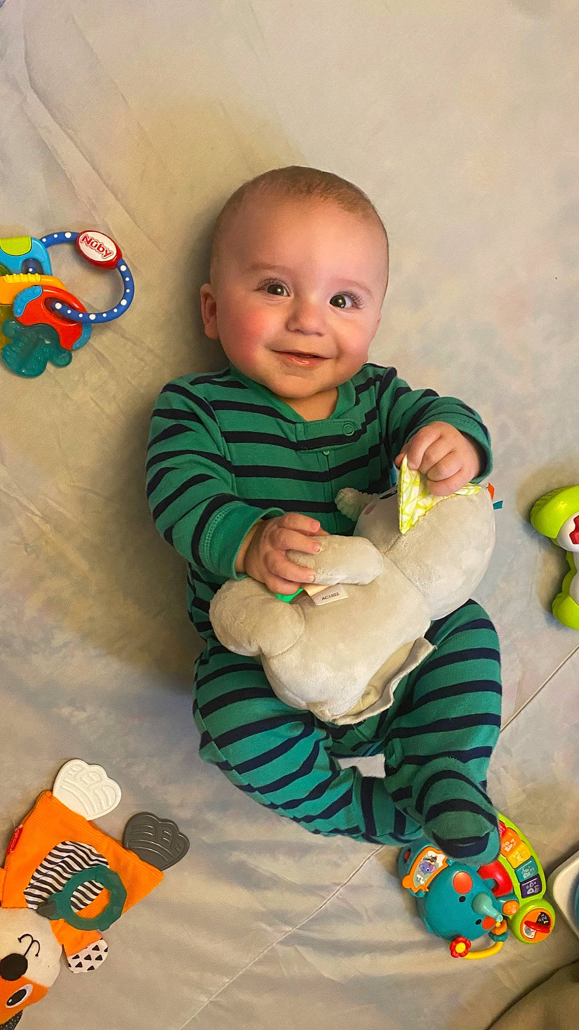 Weiland is registered to the contest to win money with this photo: arm, baby, baby_playing_with_toys, baby_toddler_clothing, cheek, child, facial_expression, finger, fun, green, happy, head, human_body, joy, organ, person, product, skin, sleeve, smile