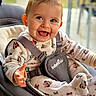 baby, smile, onesie, baby_rocker, happy, child, infant, clothing, seat, straps, indoor, cute, playful, face, hands, footwear, expression, person, young_child, comfort