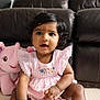 baby, child, pink_dress, stuffed_animal, elephant_toy, indoor, leather_couch, curly_hair, floor, cute, portrait, smiling, seated, young_child, playful, soft_toy, home, person, happy, decor