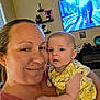 woman, baby, smile, indoor, person, face, clothing, holding, living_room, television, furniture, plant, shelf, portrait, skin, expression, casual, home, family, cute