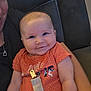 baby, infant, smile, orange_clothing, onesie, pacifier_clip, person, arm, couch, indoor, happy, child, face, seated, young, cute, skin, human, closeup, comfort
