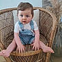 baby, blue_eyes, blurred, child, cute, floor, furniture, homedecor, indoor, overalls, pampas_grass, person, plant, portrait, seat, sitting, toddler, white_shirt, wicker_chair, wooden_floor