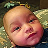 Rj is registered to the contest to win money with this photo: baby, infant, child, portrait, face, wide_eyes, looking_at_camera, indoors, blanket, patterned_blanket, blue_clothing, onesie, toys, furniture, bed, soft_lighting, close_up, sitting, head, home