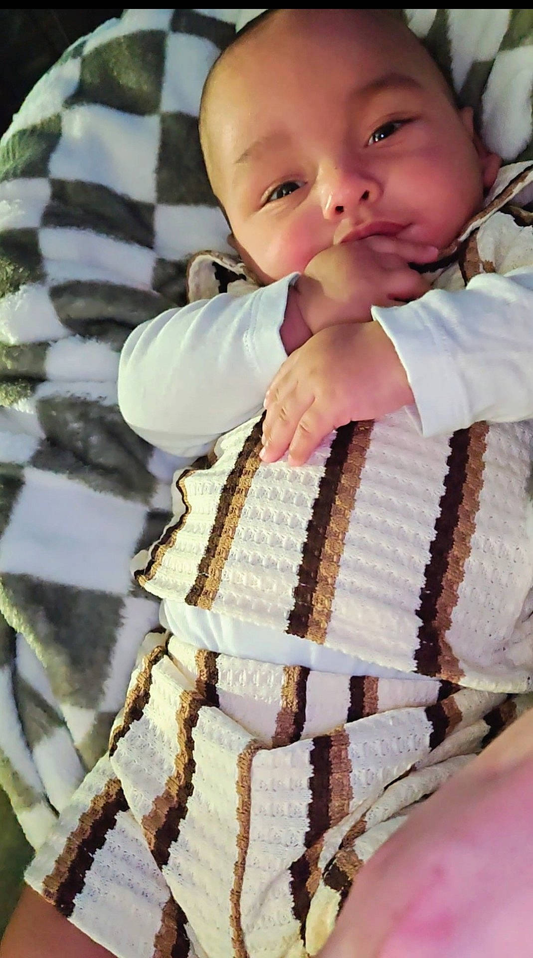 Rj is registered to the contest to win money with this photo: adorable, baby, bed, blanket, child, closeup, cozy, face, fingers, hand, indoors, infant, long_sleeves, lying_down, photography, portrait, smiling, striped_blanket, swaddled, white_clothing