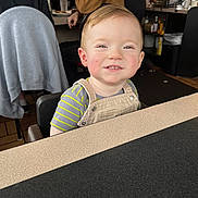 Grayson joined the competition — help win amazing prizes! toddler, child, smiling, face, high_chair, striped_shirt, overalls, restaurant, table, indoor, people, seated, casual_clothing, happy, light, hair, skin, cheeks, furniture, background