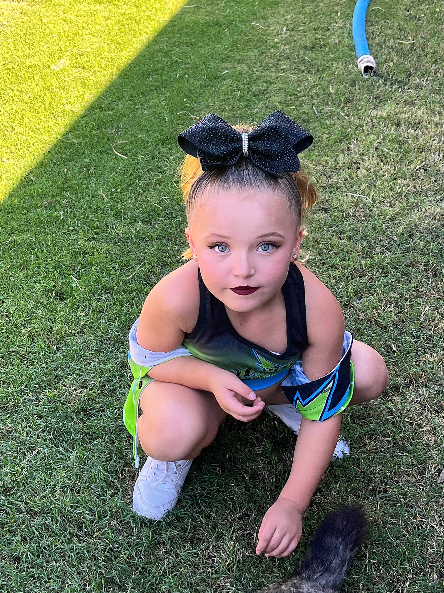 Abriella is registered to the contest to win money with this photo: child, girl, grass, outdoor, sporty_outfit, white_sneakers, black_bow, makeup, blue_eyes, squatting, animal_tail, pet, sunlight, greenery, cute, playful, young, fashion, portrait, casual